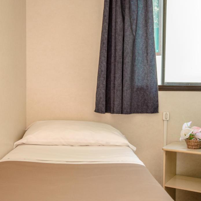 Small room with single bed, window, and nightstand with a flower basket.