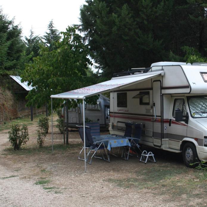 Ein Wohnmobil, das in einem bewaldeten Gebiet mit Außensitzgelegenheiten geparkt ist.