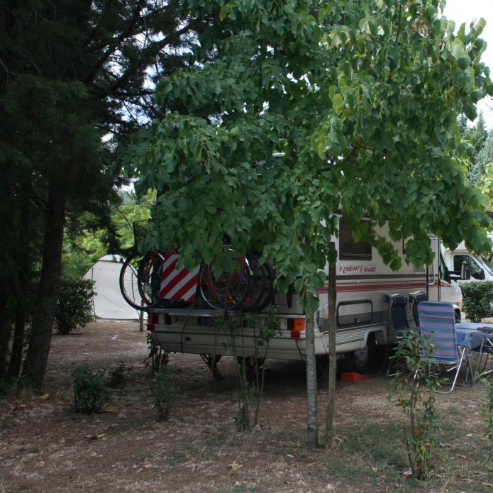Wohnmobil auf Campingplatz mit Stühlen und Tisch im Freien, Fahrräder hinten.